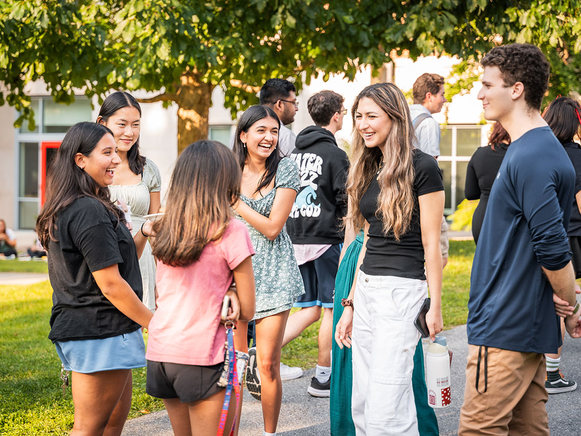 A group of smiling college students stands in a circle outside and talks